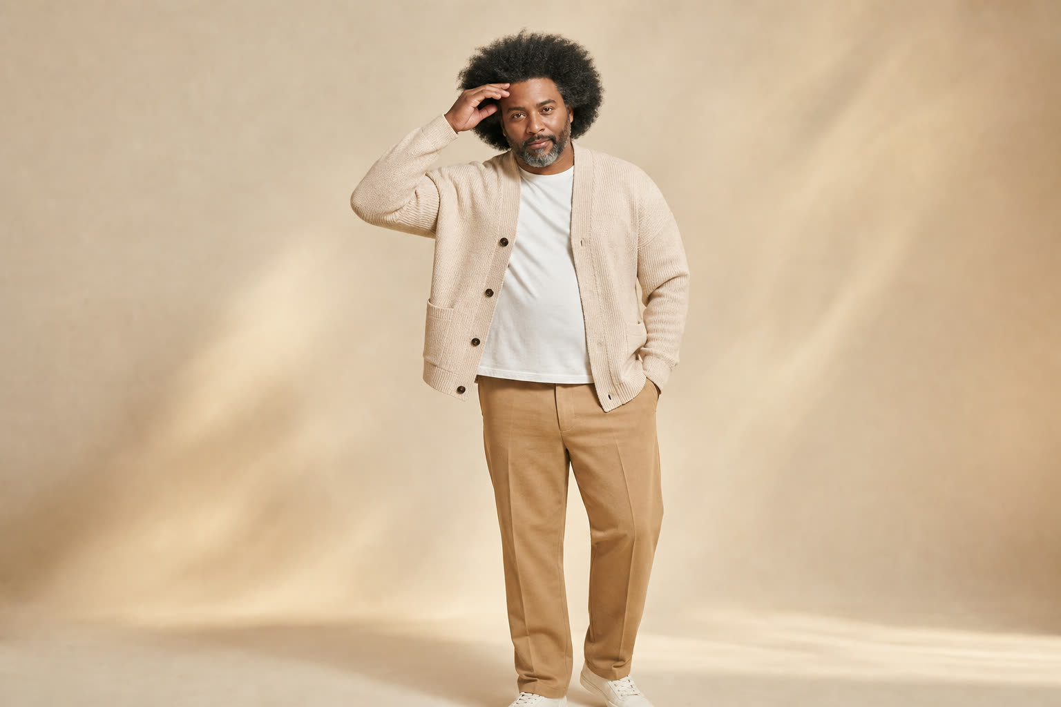 A broad, sturdy man in his 40s with a full textured afro, touching his hairline with quiet pride