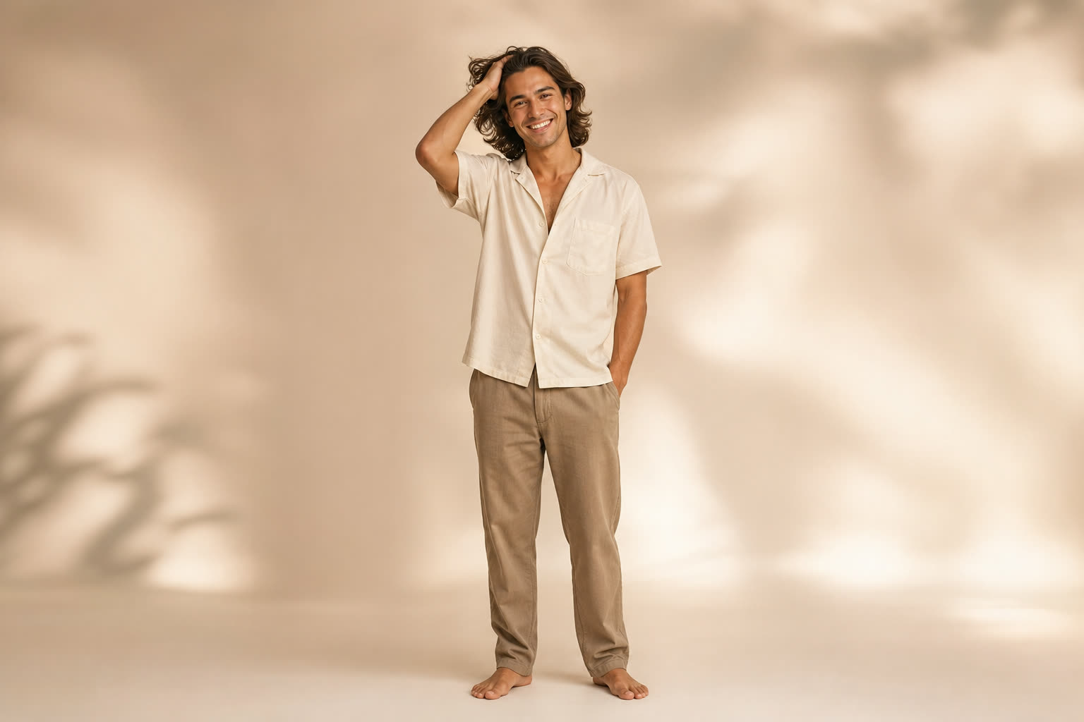 A man in his 20s with shoulder-length hair pushed back by his hand, smiling wide