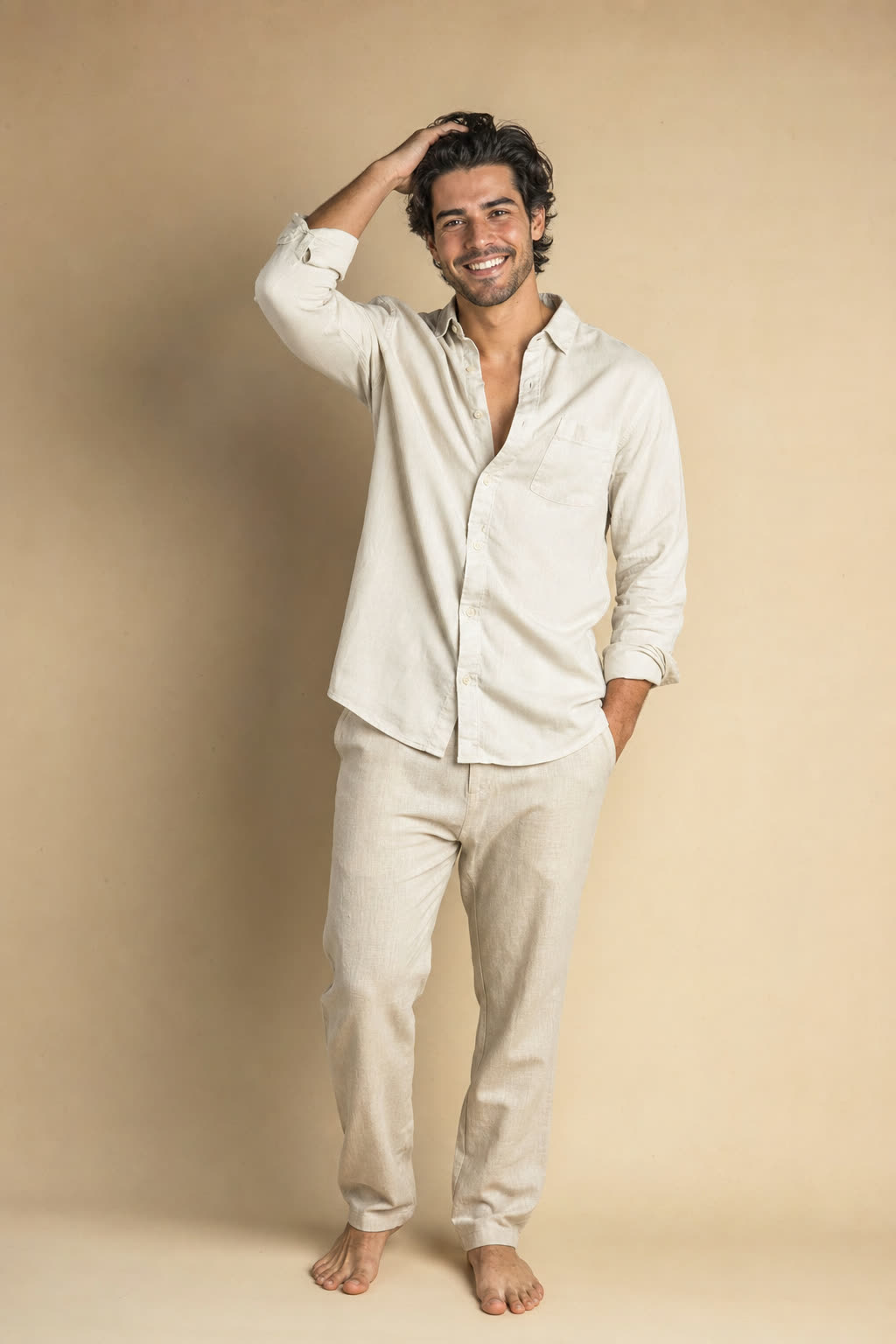 A happy man runs both hands through his thick wavy hair, whole face lifted in warm light