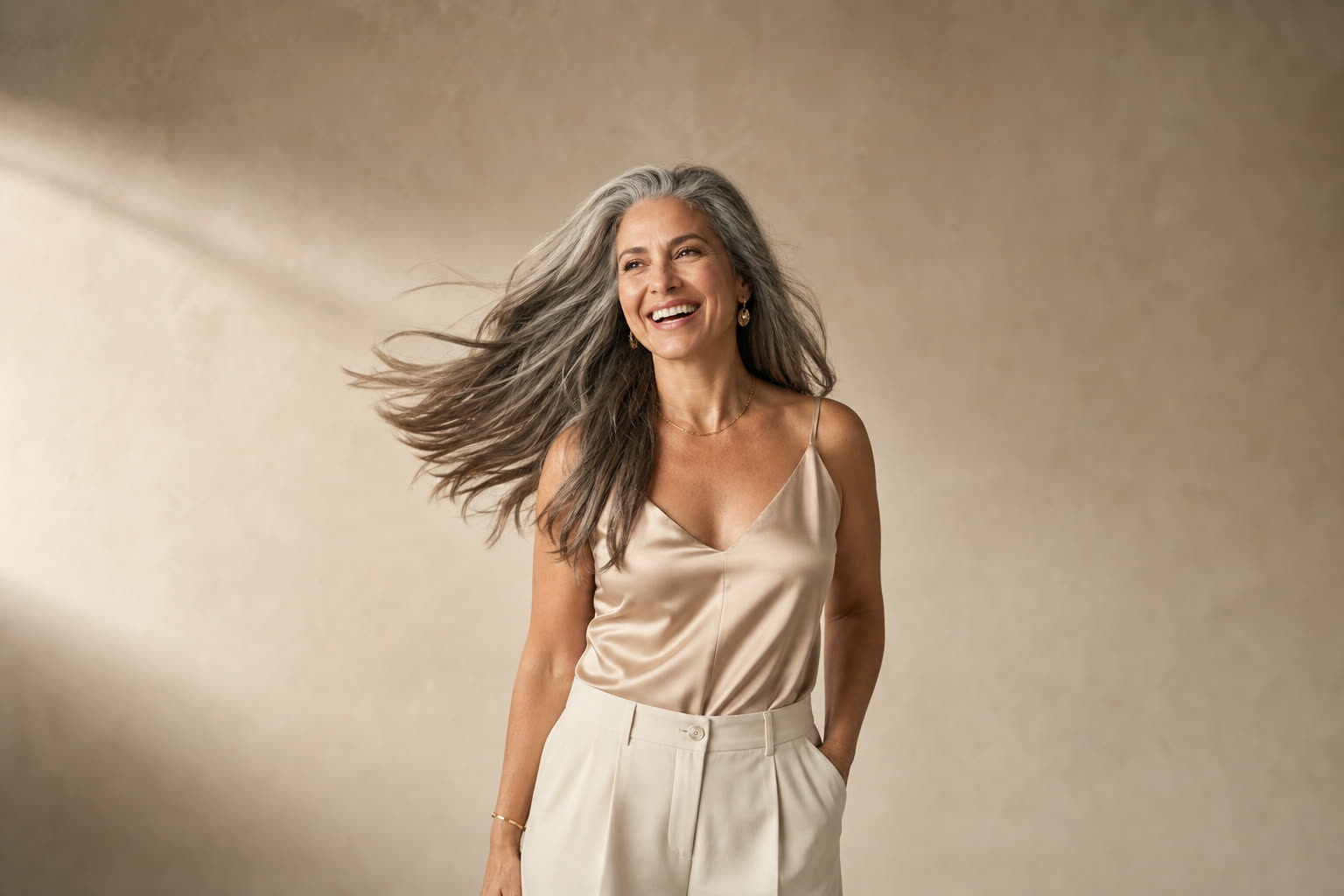 A woman in her 40s with long silver-streaked hair mid-swish, laughing