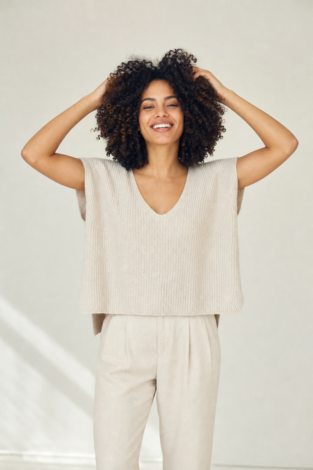 A woman with voluminous natural curls runs her fingers through her hair, eyes bright with delight