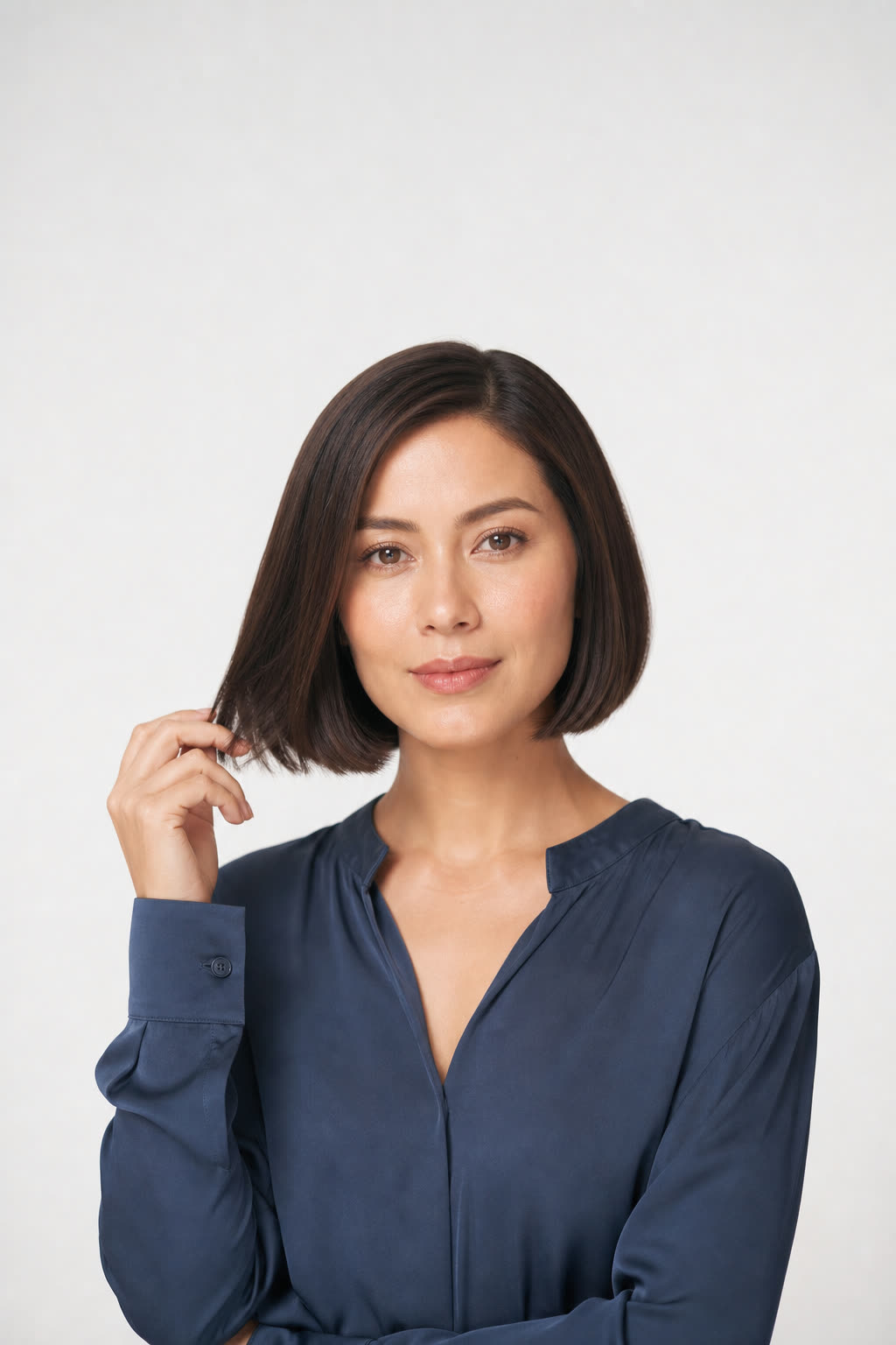 A woman with a glossy precision bob touches the ends of her hair in a minimal bright studio