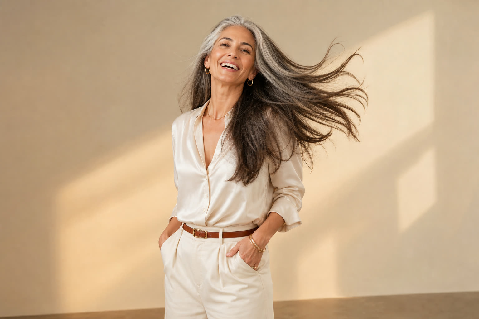 A woman in her 40s with long silver-streaked hair mid-swish, laughing