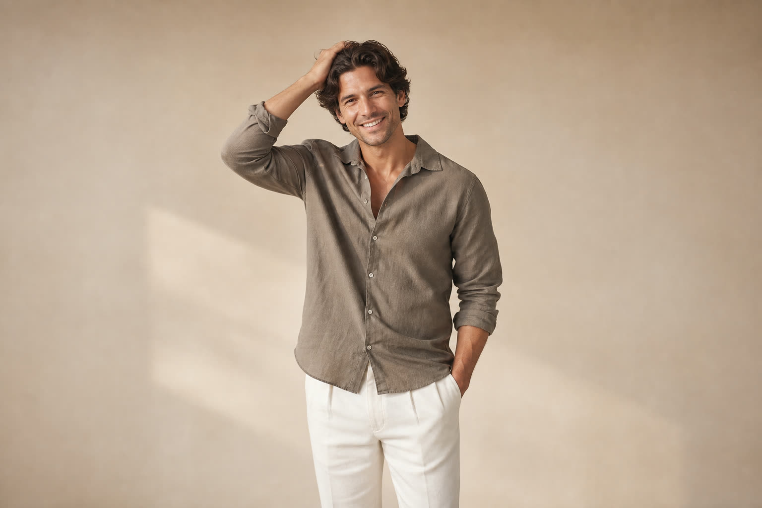A man in his 30s with thick wavy hair, running one hand through it with an easy grin