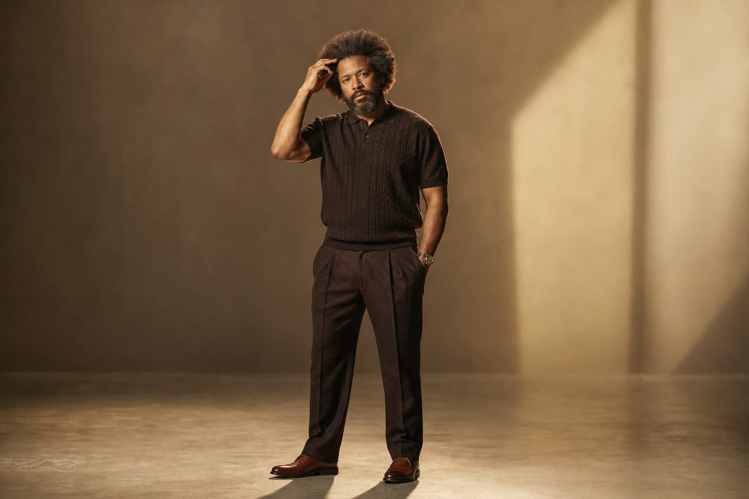 A broad, sturdy man in his 40s with a full textured afro, touching his hairline with quiet pride