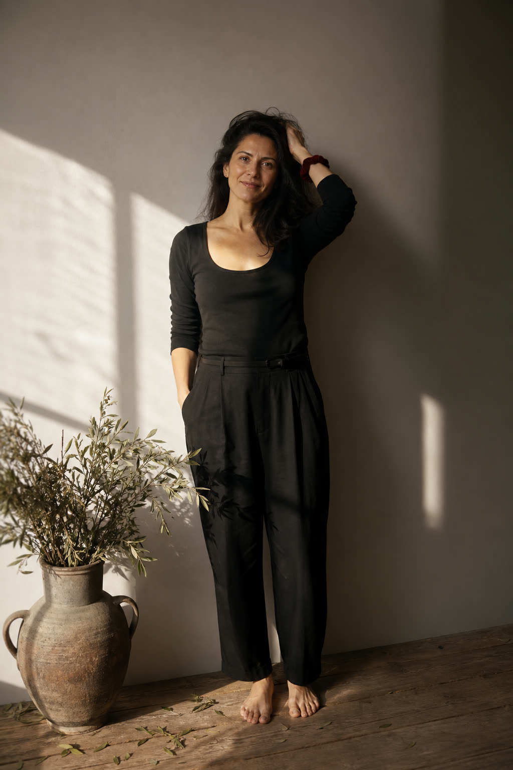 A woman in her 30s brushing back full dark hair in warm morning window light