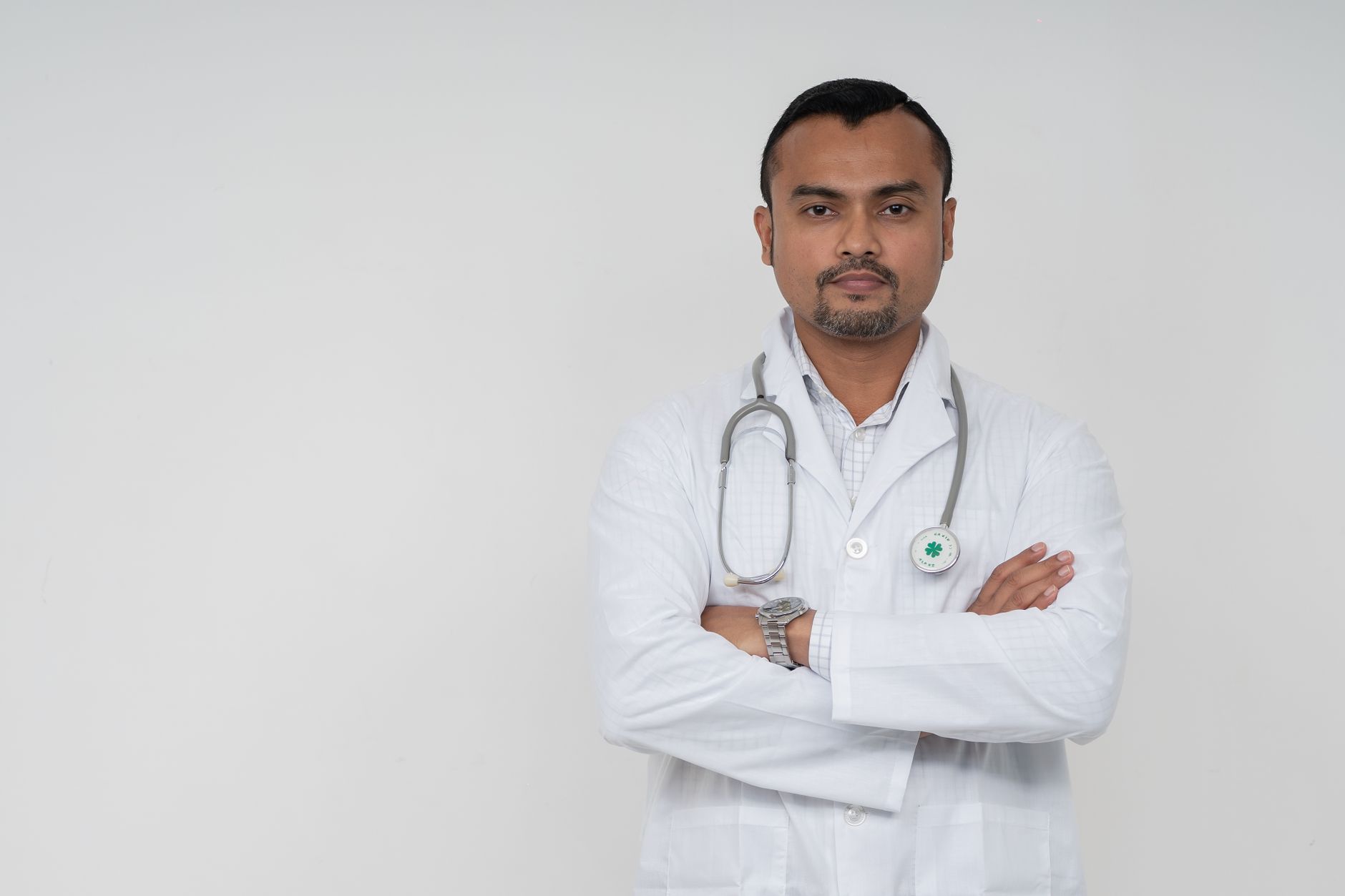 Confident South Asian male doctor in white coat with stethoscope, portrait shot.