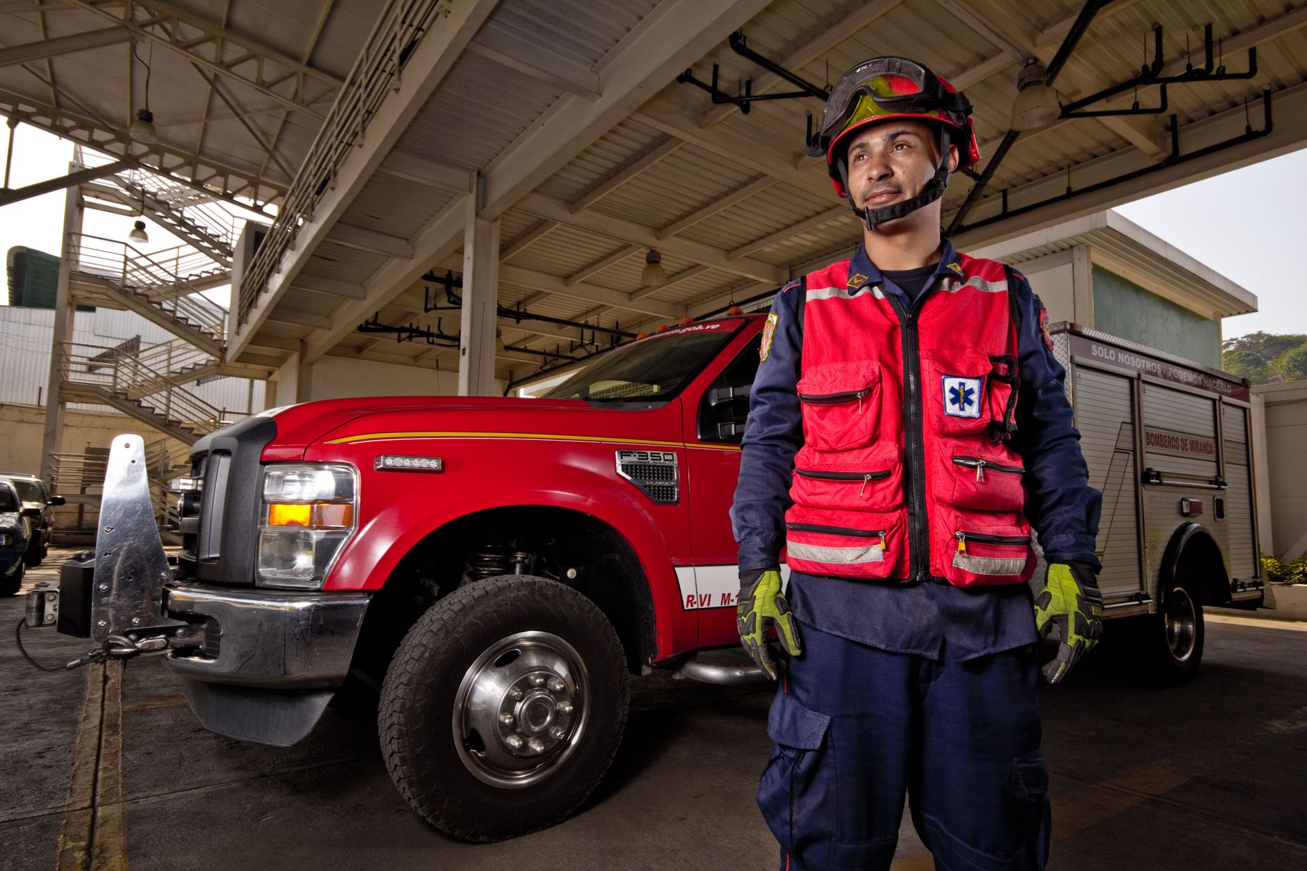 Firefighter in uniform standing confidently beside fire engine inside a station.