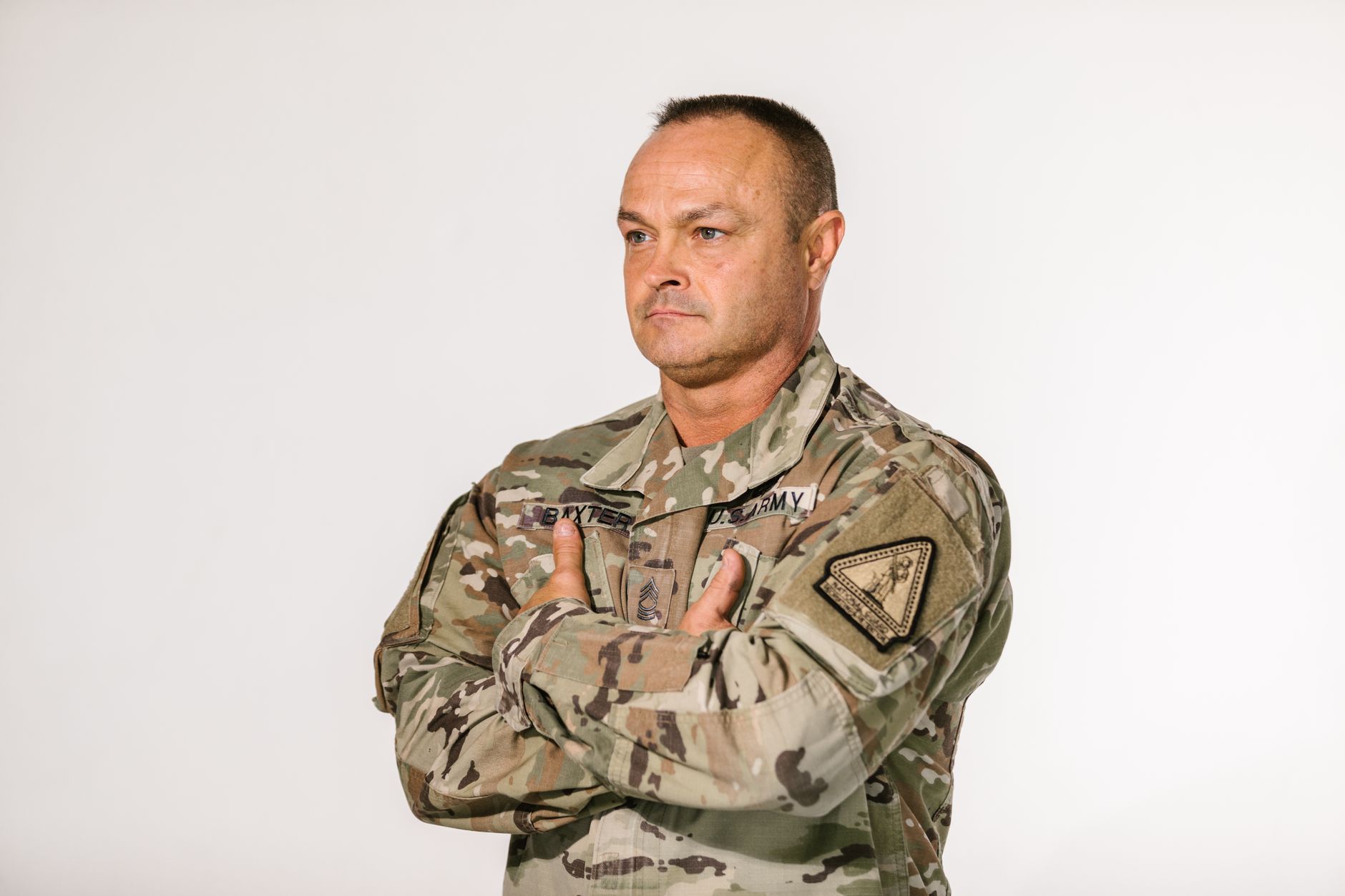 A confident military veteran in camouflage uniform poses with pride in a studio setting.
