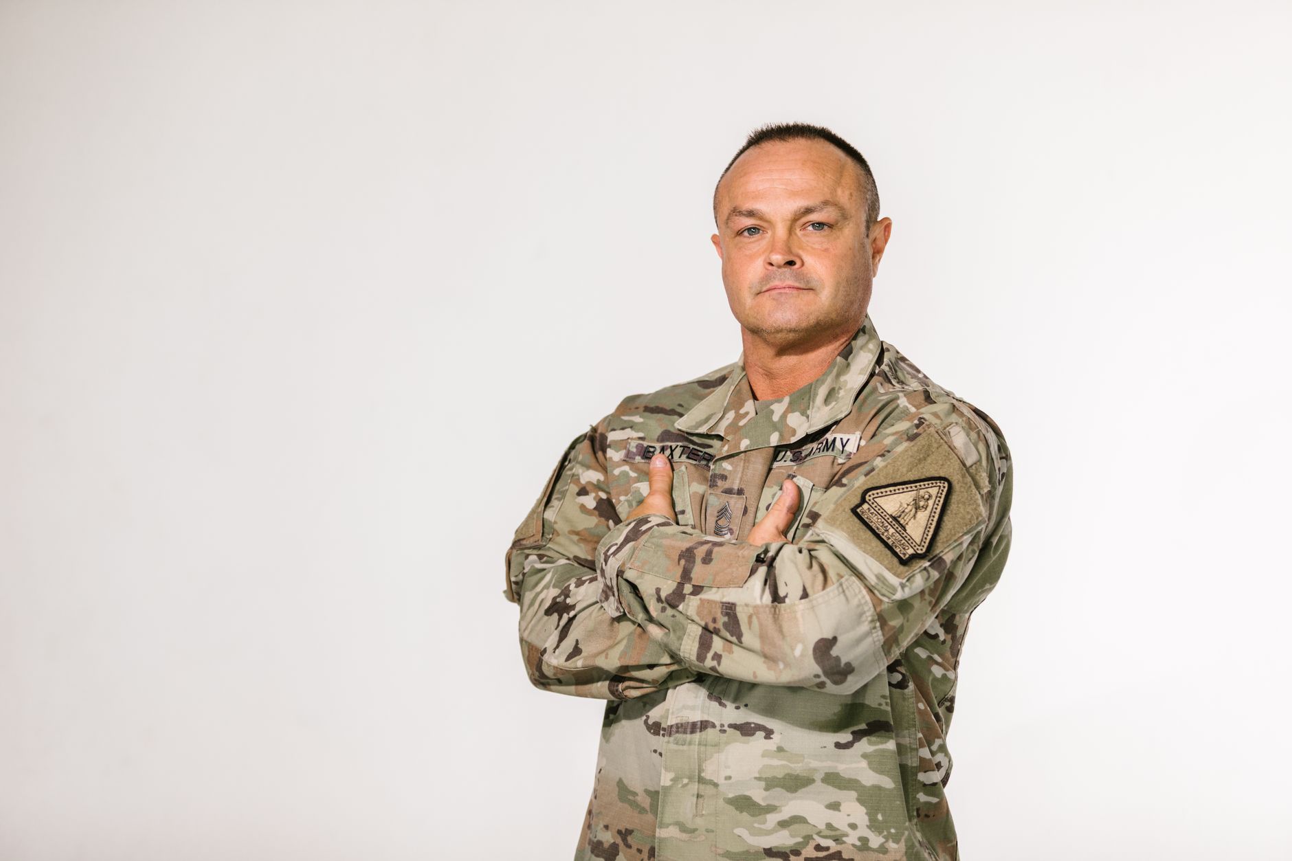 Military veteran standing with pride in camouflage uniform against a white background.