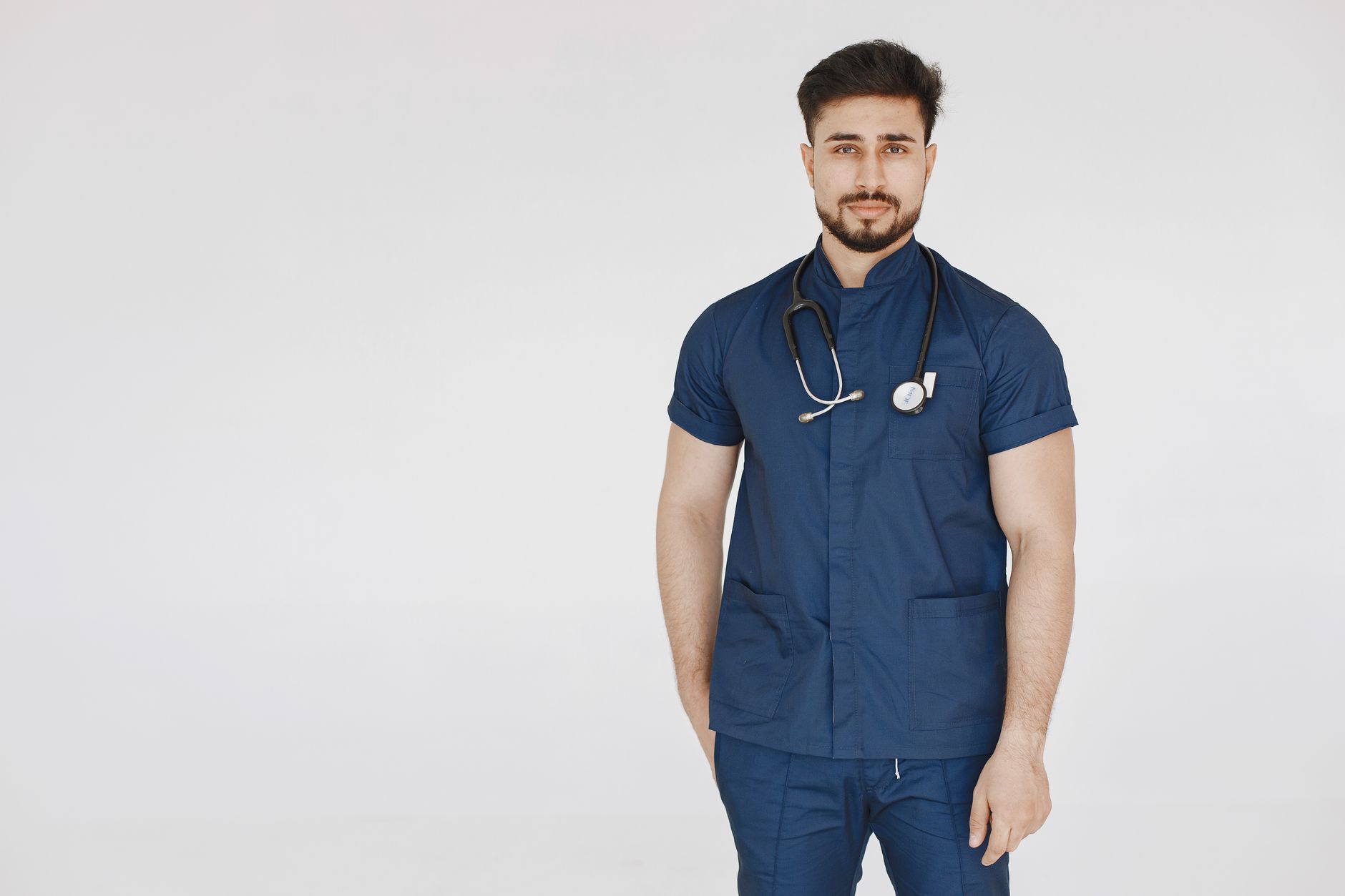 Confident male doctor in blue scrubs with stethoscope against white background.