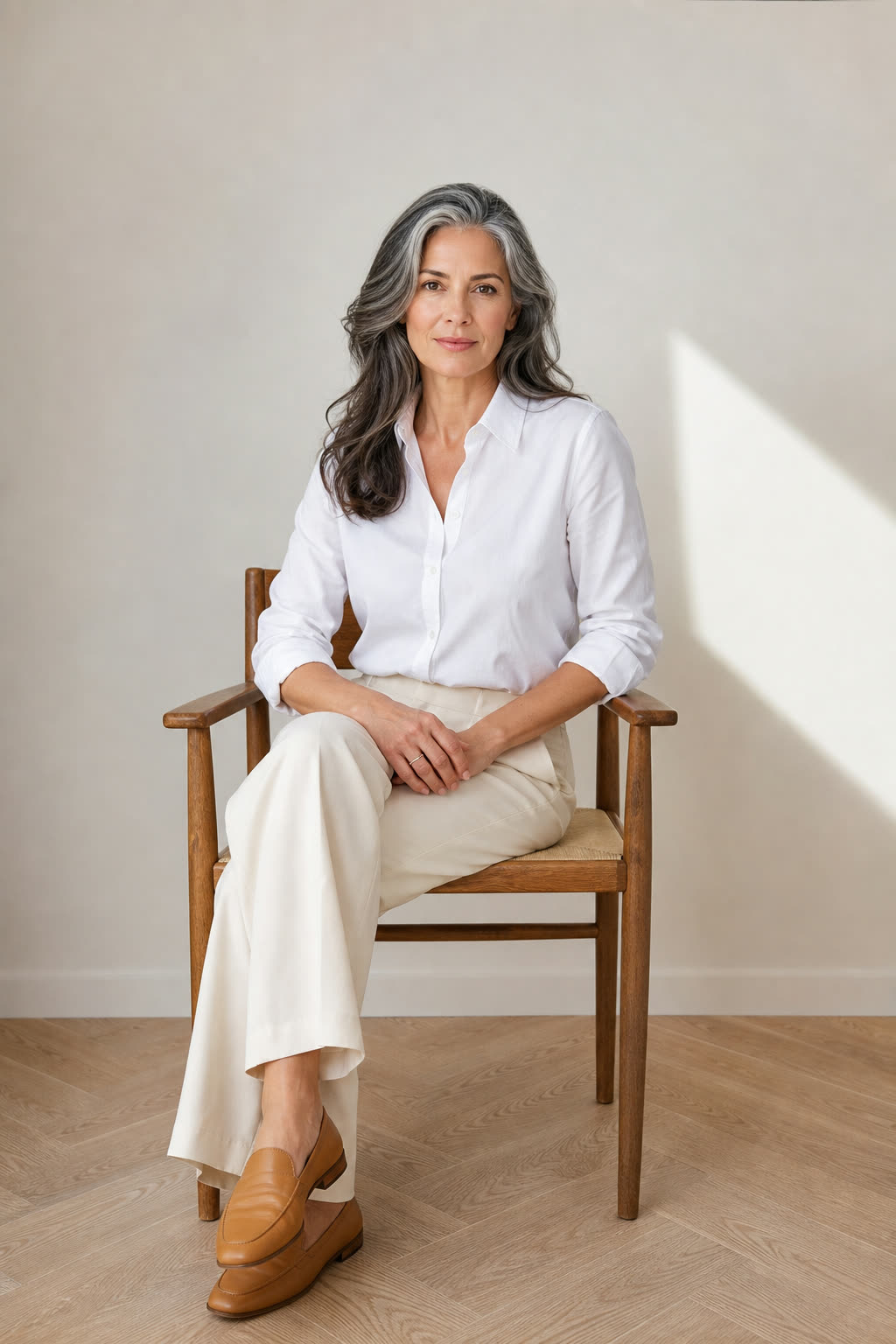 A woman in a crisp white shirt meets the camera with a calm, direct gaze, whole face lit evenly against a pale wall
