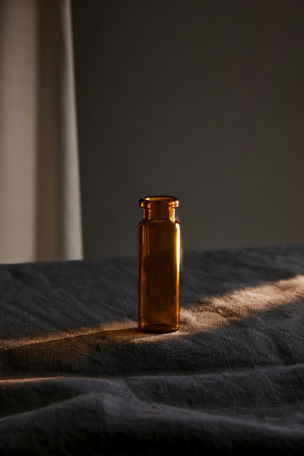 A single amber medication vial stands on dark linen, caught in one dramatic beam of light
