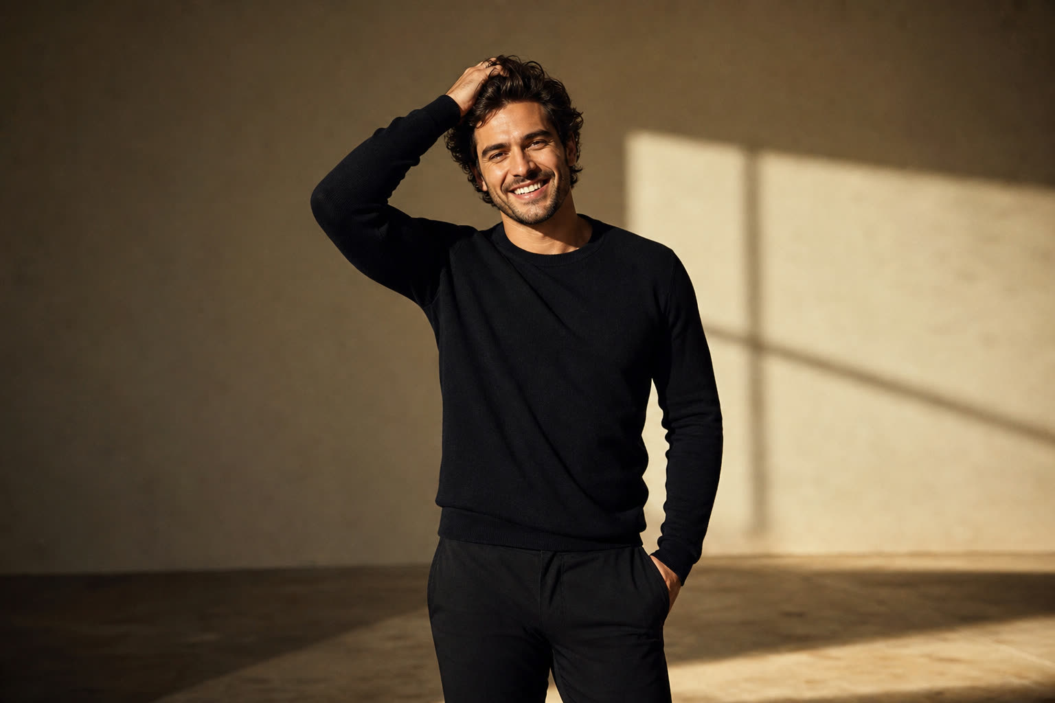 A man in his 30s with thick wavy hair, running one hand through it with an easy grin