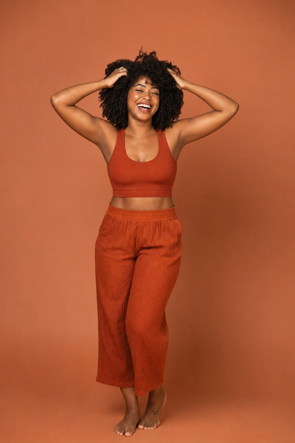 A person runs both hands through thick, healthy hair, laughing in warm daylight