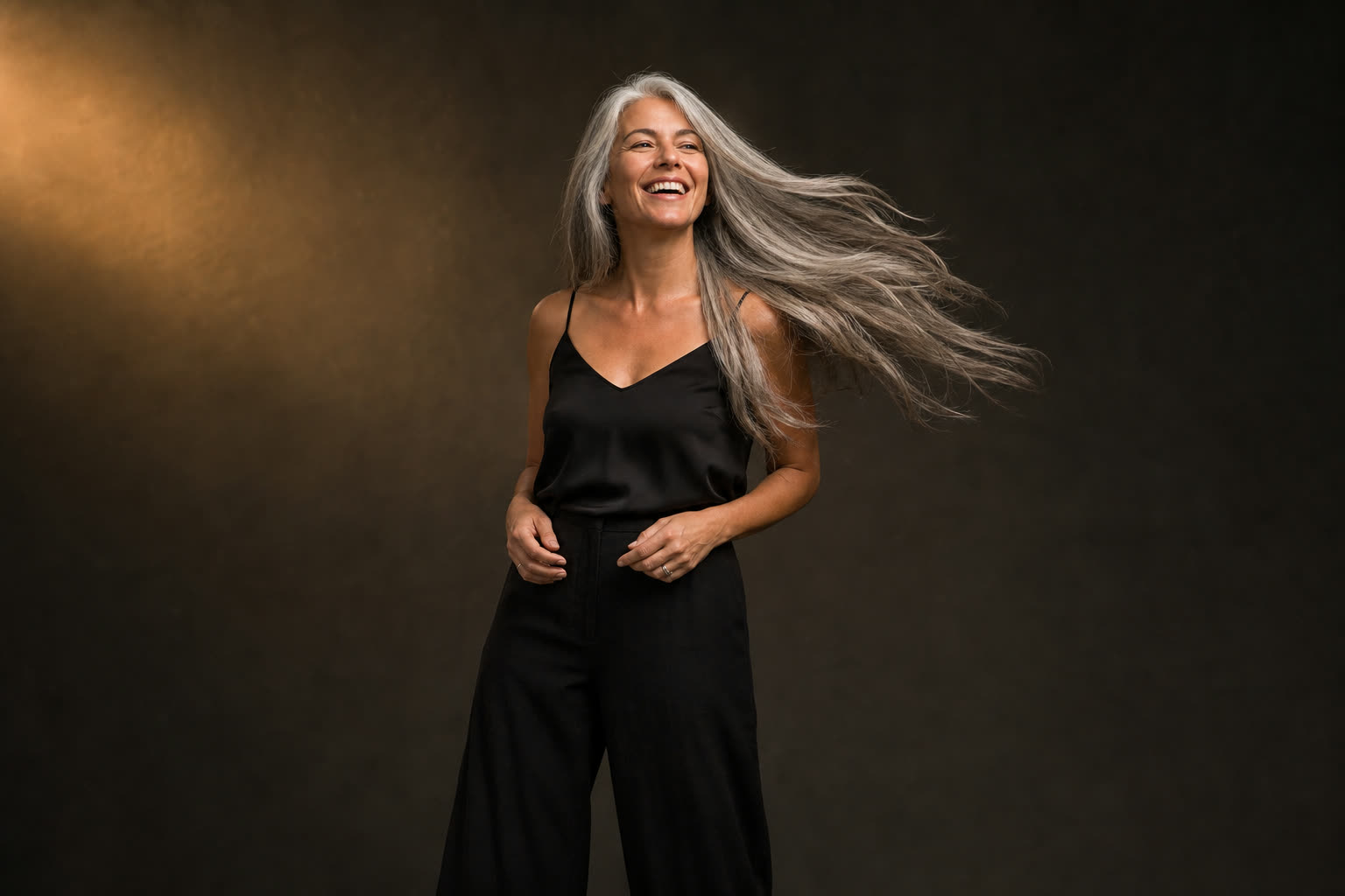 A woman in her 40s with long silver-streaked hair mid-swish, laughing