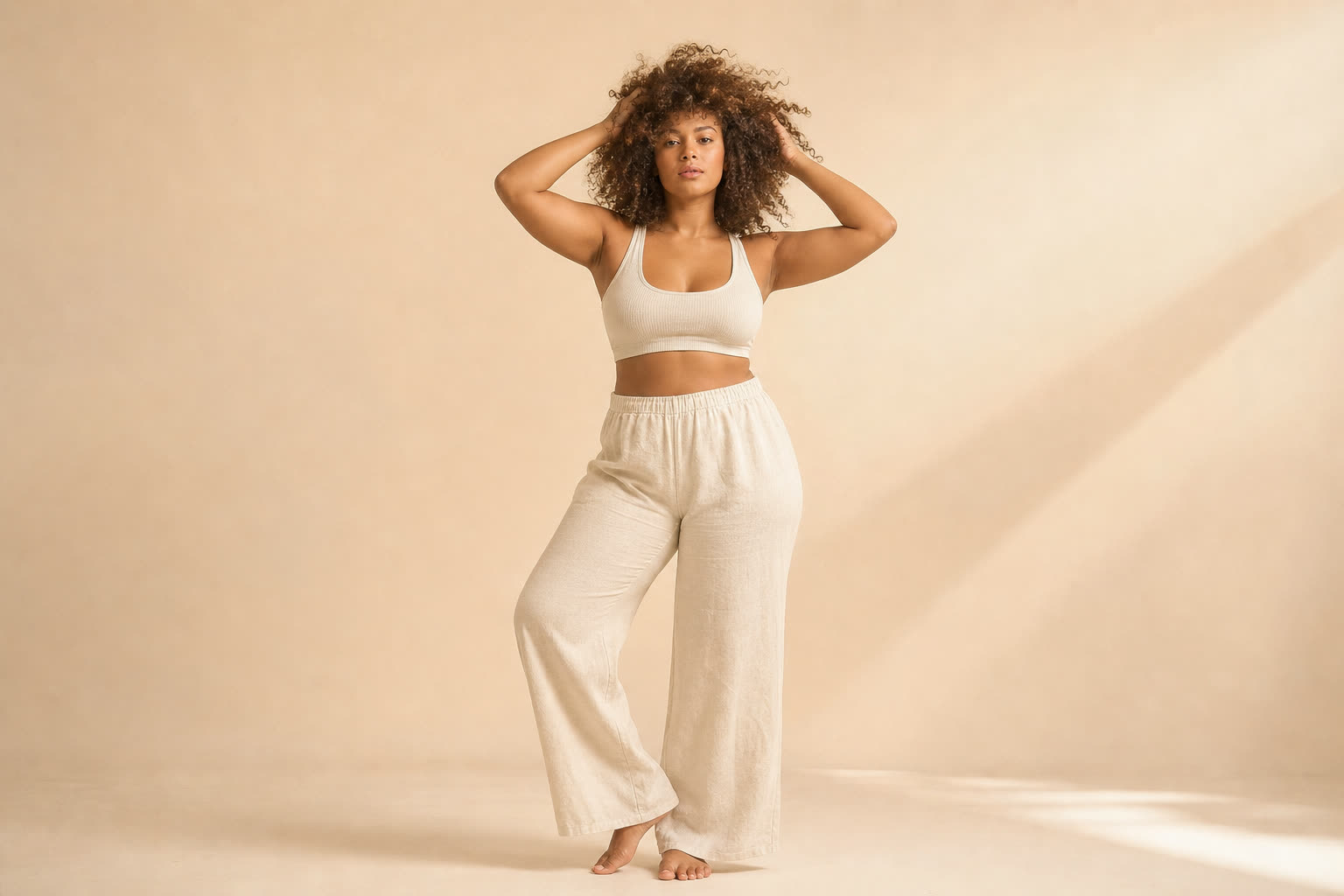 A woman in her 20s with a soft curvy build and glorious tight curls, both hands lifted into her hair