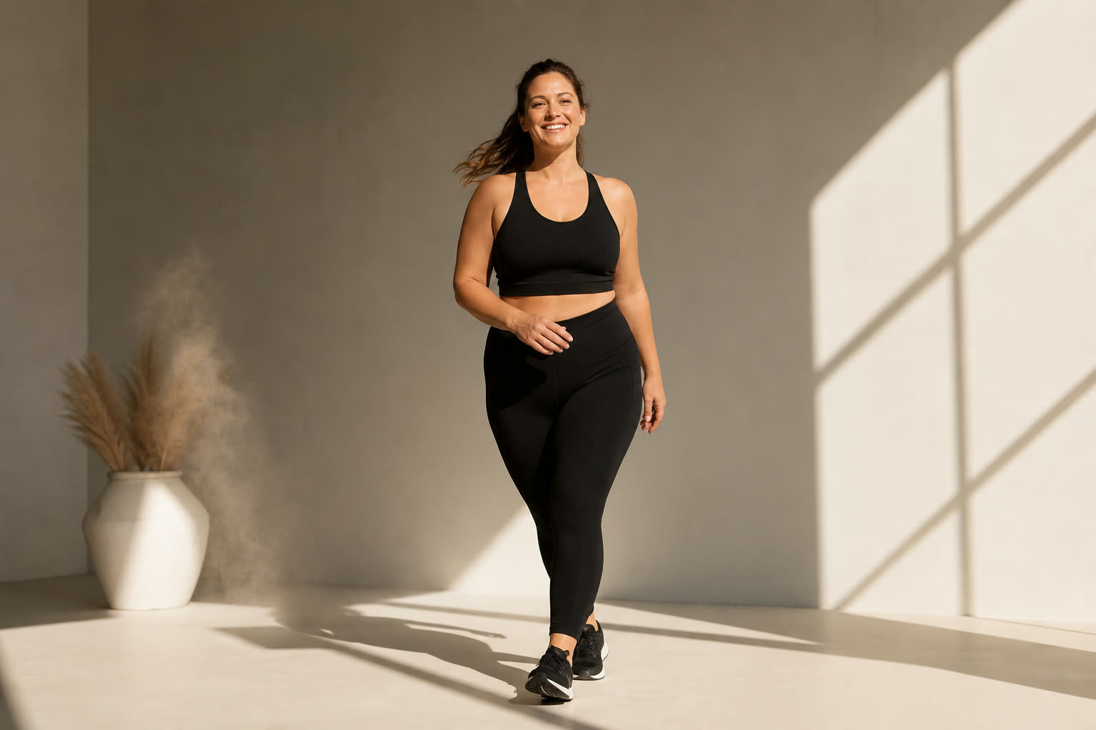 A woman with a soft, strong build mid-stride across a white studio floor slashed with warm light