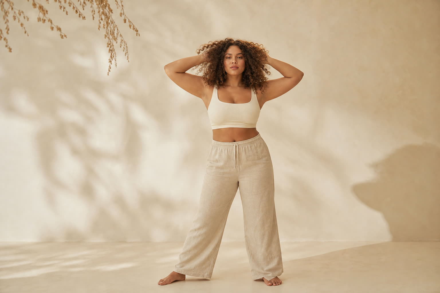 A woman in her 20s with a soft curvy build and glorious tight curls, both hands lifted into her hair