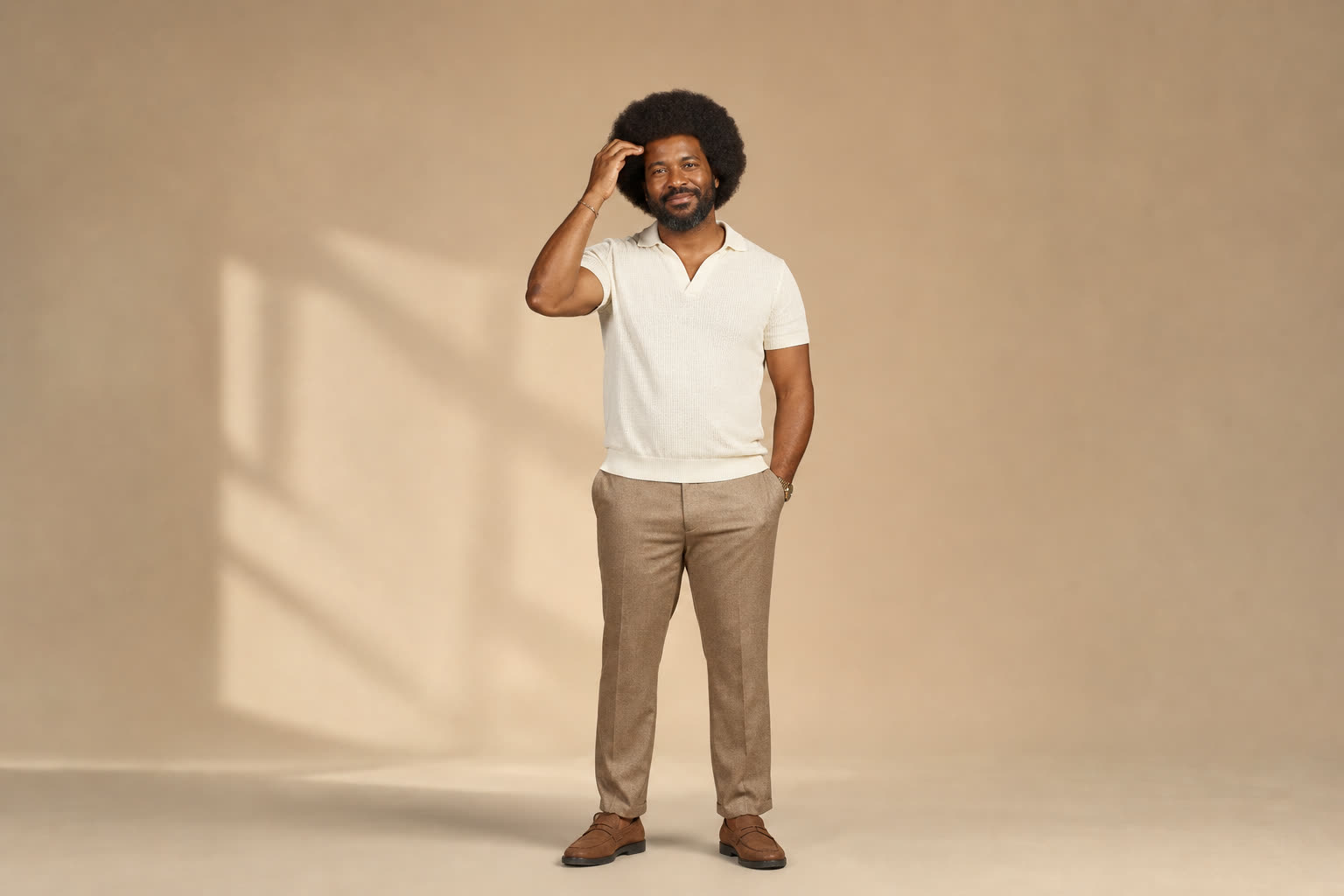 A broad, sturdy man in his 40s with a full textured afro, touching his hairline with quiet pride