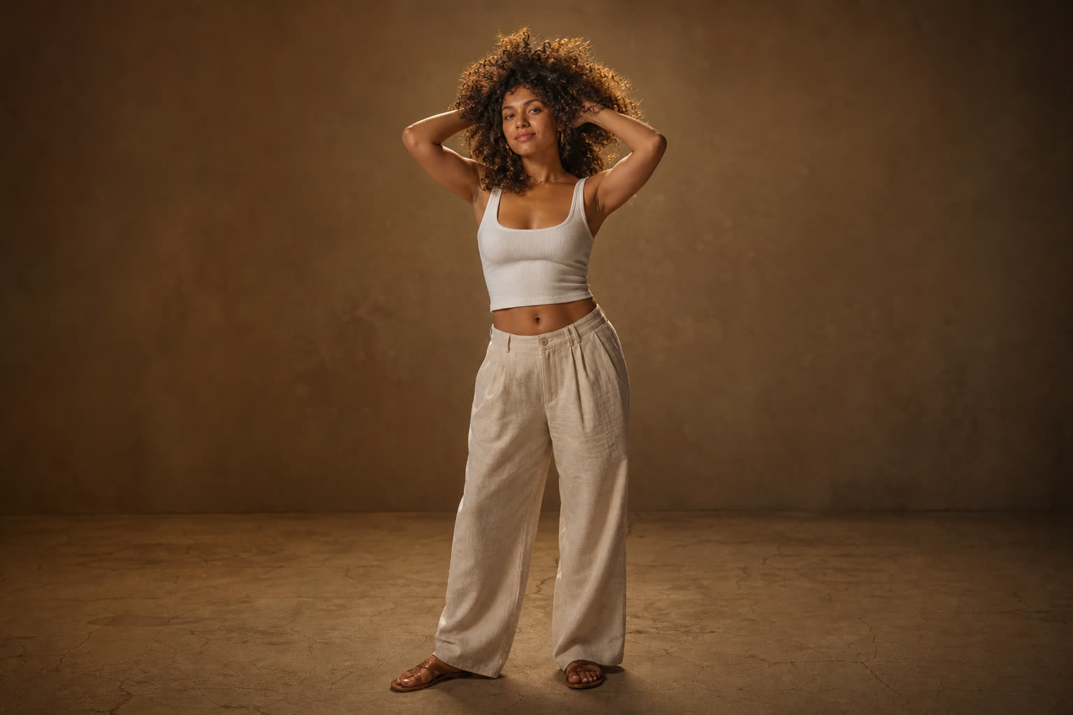 A woman in her 20s with a soft curvy build and glorious tight curls, both hands lifted into her hair