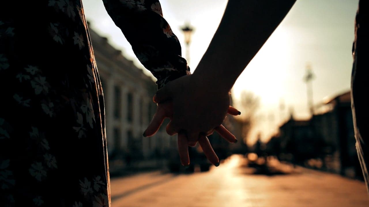 A couple holding hands on a warm evening street at sunset