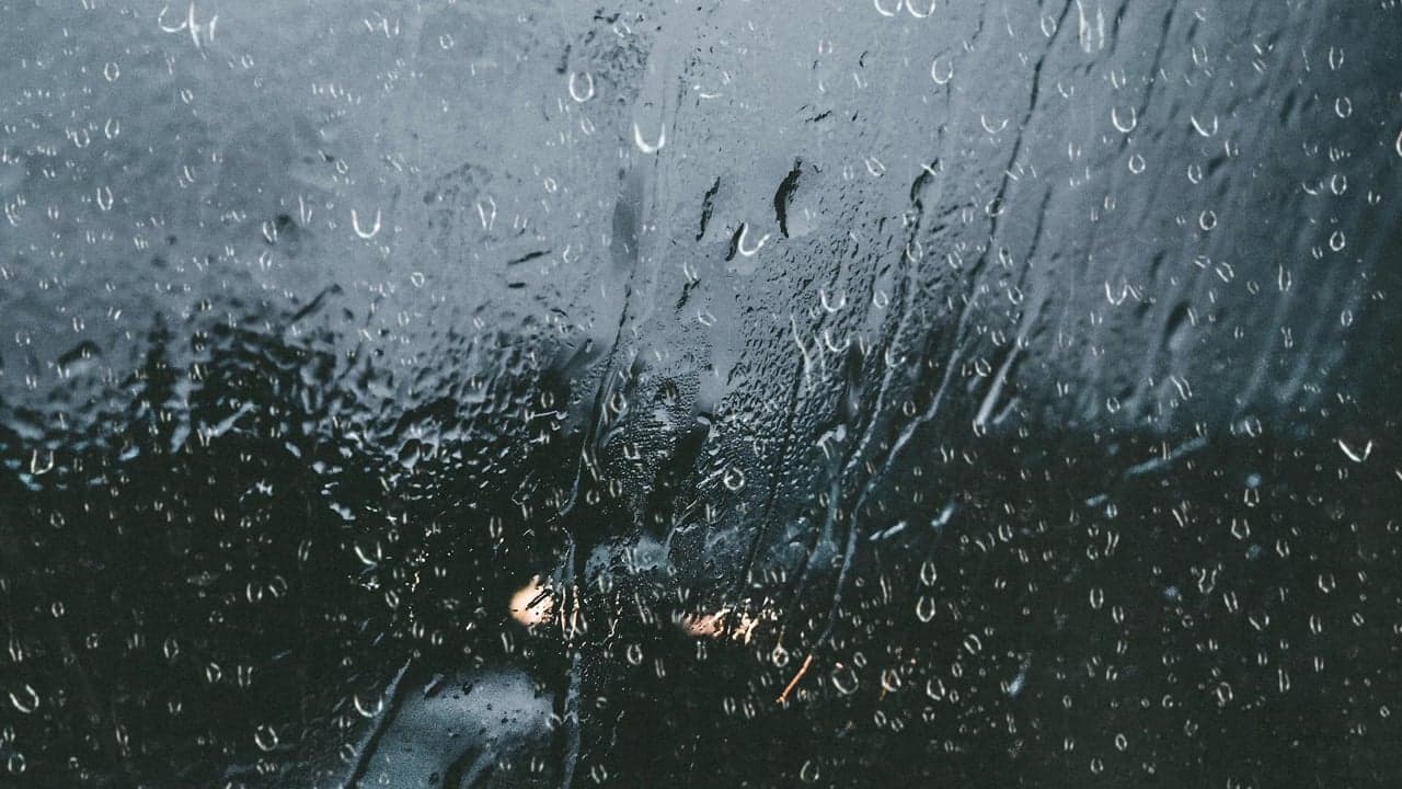 Rain sliding down a window at night, city lights beyond