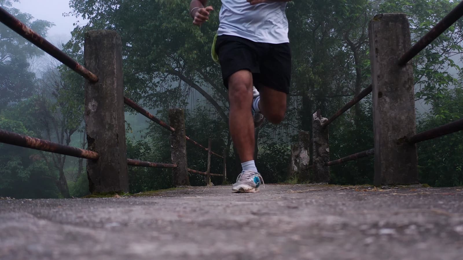 A man jogging across a misty bridge trail in the early morning