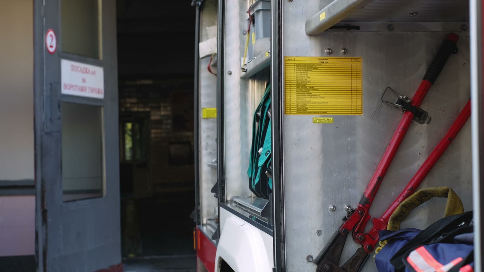 Two firefighters lifting equipment down from the back of an engine inside a station